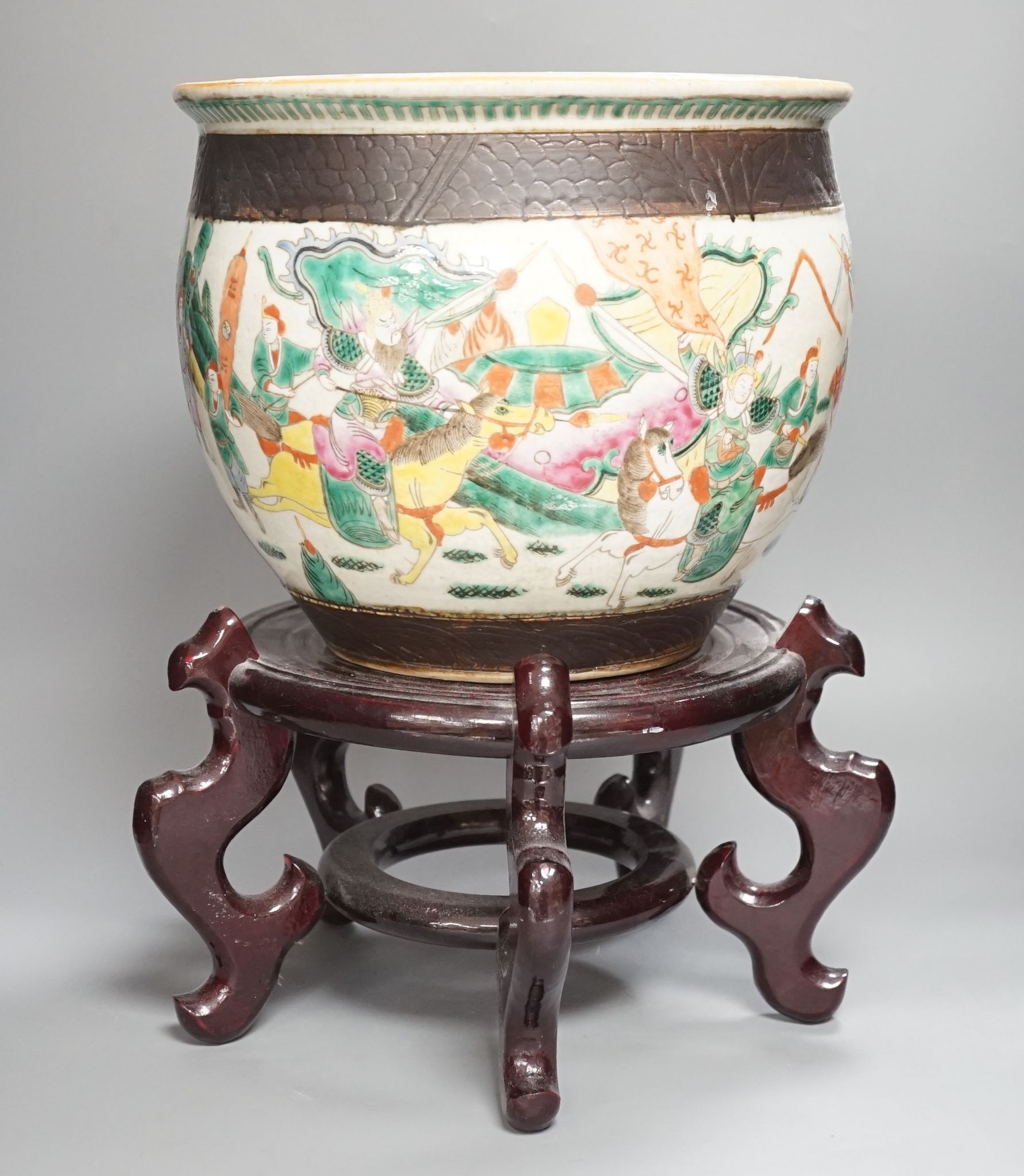 A Chinese famille rose ‘warriors’ jardiniere, late 19th century, wooden stand, 42 cms high including stand.